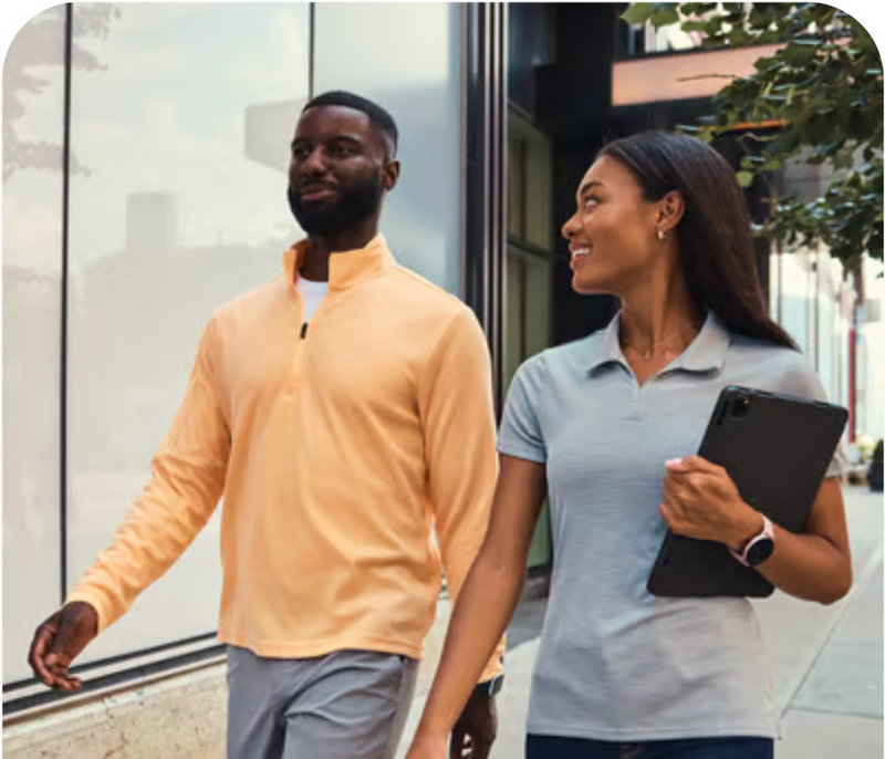 Two people walking on a sidewalk, one holding a tablet.